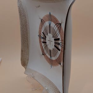 Peut inclure: Un plat de service en céramique blanc cassé vintage avec une forme incurvée unique. Le plat présente un motif circulaire central marron, noir et bleu, avec un motif en étoile. Les bords ont un aspect craquelé et vieilli, ajoutant à son charme rétro.