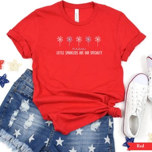 May include: Red t-shirt with a graphic of fireworks and the text "Little sparklers are our specialty".