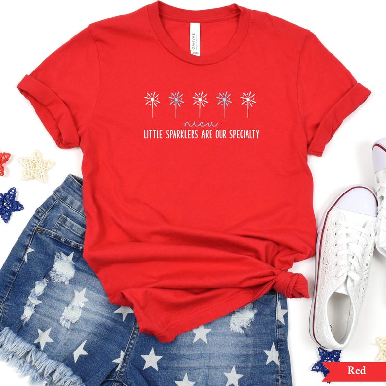 May include: Red t-shirt with a graphic of fireworks and the text "Little sparklers are our specialty".