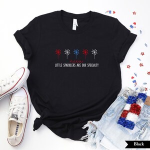 May include: Black t-shirt with a red, white, and blue firework design and the text "Little Sparklers Are Our Specialty".