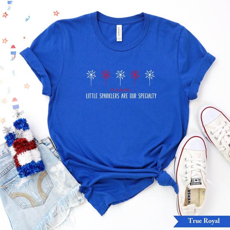May include: A royal blue t-shirt with a red, white, and blue firework design and the text "Little Sparklers Are Our Specialty".