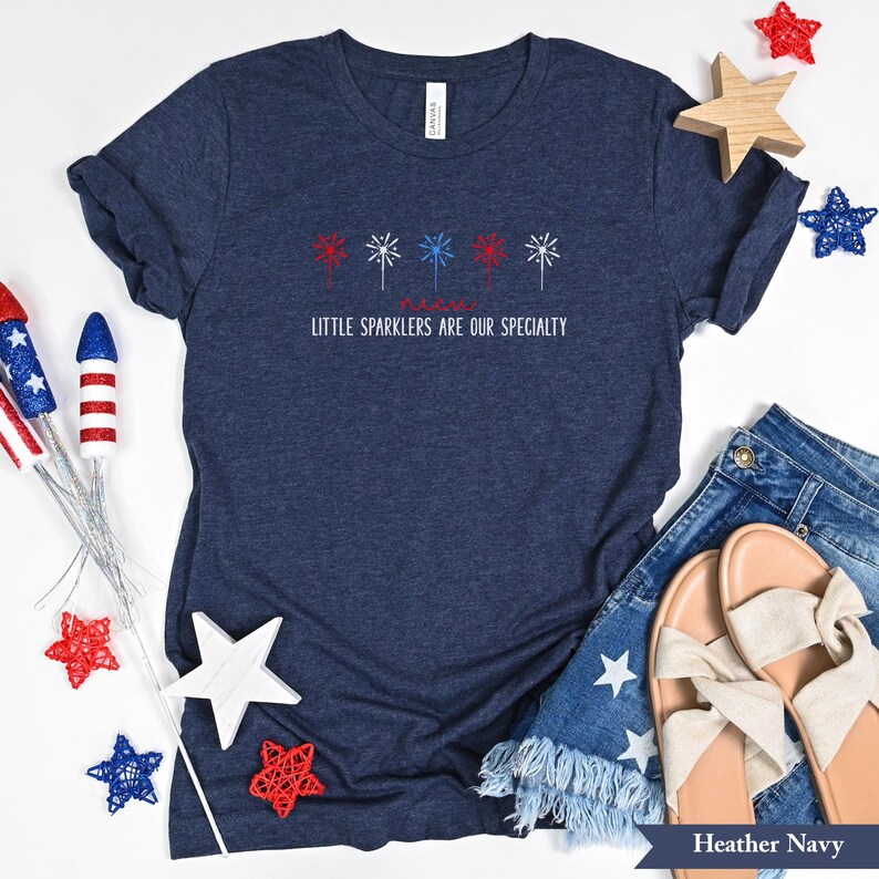 May include: A navy blue t-shirt with a red, white, and blue firework design and the text "Little Sparklers Are Our Specialty".