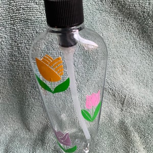 May include: A clear glass pump bottle with a black pump top. The bottle has a floral design with yellow, pink, and purple tulips.