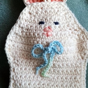 May include: White crocheted bunny with pink ears, blue and green bow, and a blue and green ruffled trim.