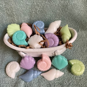 May include: A white ceramic bathtub filled with colorful seashell-shaped bath bombs. The bath bombs are in shades of blue, green, pink, and white.