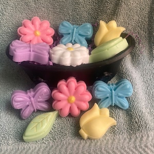 May include: A collection of colorful handmade soap bars shaped like flowers and butterflies. The soaps are arranged in a small black bathtub.