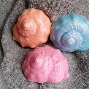 May include: Three decorative seashells in different colors: pink, blue, and peach. Each shell has a spiral design and a glittery finish.