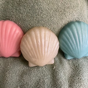 May include: Three decorative seashell-shaped soaps in pink, white, and blue with a glittery finish.