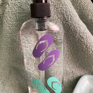 May include: A clear glass bottle with a black pump dispenser. The bottle has purple and teal flip-flop stickers on it.
