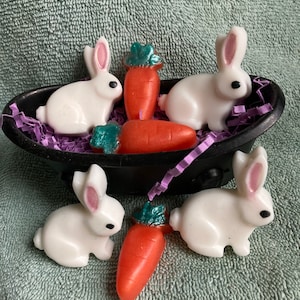 May include: Five white bunny shaped soaps and three orange carrot shaped soaps. The soaps are in a black tub with purple shredded paper.