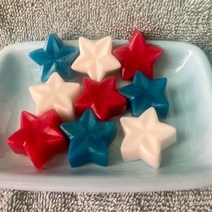 May include: A collection of nine star-shaped soaps in red, white, and blue colors. The soaps are arranged on a light blue rectangular dish.