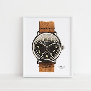 Puede incluir: Una impresi&oacute;n enmarcada en blanco de una ilustraci&oacute;n en blanco y negro de un reloj Shinola con una correa de cuero marr&oacute;n. La esfera del reloj tiene n&uacute;meros y manecillas blancos. El texto "Shinola Detroit" est&aacute; impreso en la esfera del reloj. El texto "Runwell" est&aacute; impreso debajo del reloj.