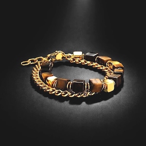 May include: A double-strand bracelet featuring a gold-toned metal chain and a strand of alternating brown tiger eye stone cubes and polished gold-toned metal cubes. The bracelet includes a gold-toned metal lobster claw clasp and an adjustable chain.