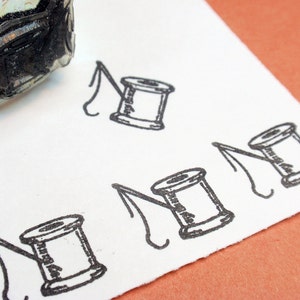 May include: A white sheet of paper with four black and white illustrations of spools of thread. Each spool has a curved line extending from it, resembling a needle.