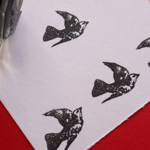 May include: A white card with four black bird stamps. The stamps are of a simple bird design with a wingspan and a small head.