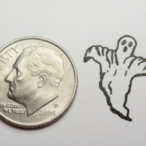 May include: A silver US dime coin with the words "LIBERTY" and "IN GOD WE TRUST" and the year "2004" on it. The coin is next to a black and white drawing of a ghost with two eyes and a mouth.
