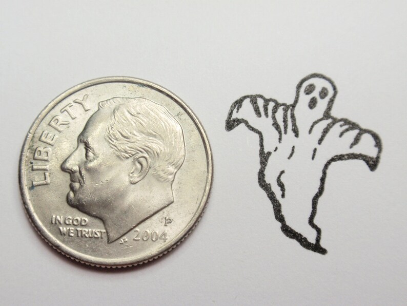May include: A silver US dime coin with the words "LIBERTY" and "IN GOD WE TRUST" and the year "2004" on it. The coin is next to a black and white drawing of a ghost with two eyes and a mouth.