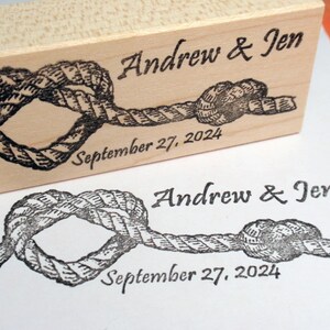 May include: A wooden stamp with a nautical rope knot design. The stamp is engraved with the names "Andrew & Jen" and the date "September 27, 2024". A stamped impression of the design is visible below.