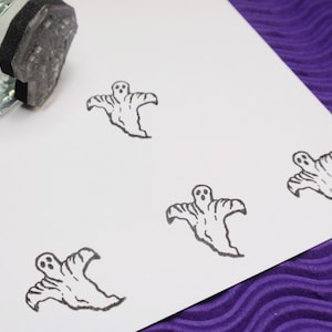 May include: A close-up of a white card with four black and white ghost stamps. The stamps are of a simple ghost design with two eyes and a mouth.