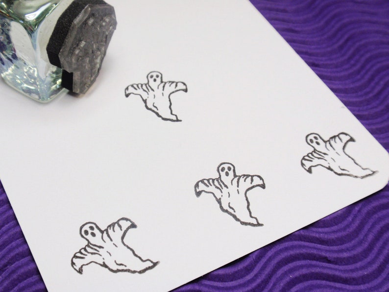 May include: A close-up of a white card with four black and white ghost stamps. The stamps are of a simple ghost design with two eyes and a mouth.