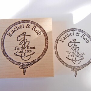 May include: A wooden stamp with a circular design featuring the names "Rachel & Rob", the phrase "Tie the Knot", and the date "7.25.2020". The design includes an anchor and rope border.