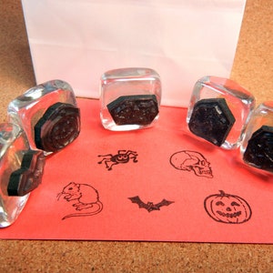 May include: Five clear glass stamp blocks with black rubber stamps inside. The stamps feature Halloween themed designs including a skull, a pumpkin, a bat, a spider, a mouse, and a geometric design.