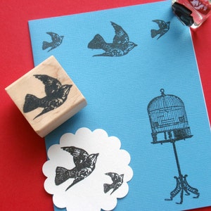 May include: A blue card with a white scalloped circle on it. The circle has a black bird design on it. The card also has a black bird design in the top right corner and a black birdcage design in the bottom right corner.