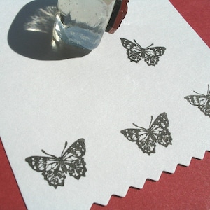 May include: A white card with four black butterfly stamps. The butterflies are in different positions on the card. The card is on a red surface.