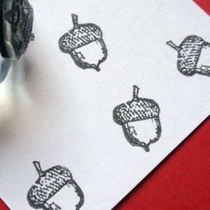 May include: A white card with four black and white acorn stamps. The acorns are drawn in a simple, stylized manner.