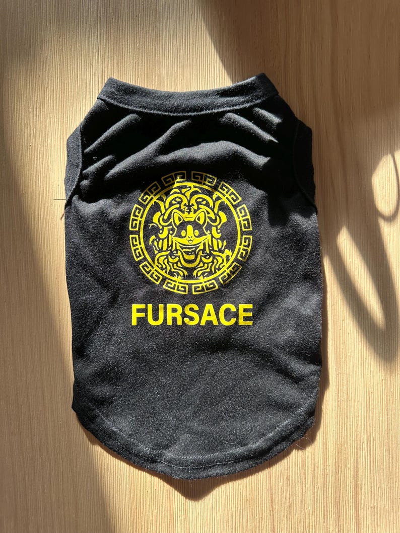 K&ouml;nnte beinhalten: Schwarzes Hunde-T-Shirt mit einem gelben, von Medusa inspirierten Grafikdesign und dem Wort "FURSACE" in Gelb. Das Shirt besteht aus einem weichen Material und ist f&uuml;r Haustiere konzipiert.