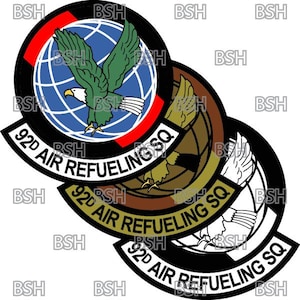 Op de afbeelding: Drie overlappende patches met zwarte randen en witte tekst. De bovenste patch is rood, wit en blauw met een wereldbol en een groene adelaar. De middelste patch is bruin met een wereldbol en een gouden adelaar. De onderste patch is zwart en wit met een wereldbol en een witte adelaar. Alle drie patches hebben de tekst "92D AIR REFUELING SQ".
