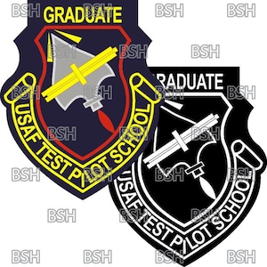 Puede incluir: Un parche blanco y negro con forma de escudo y el texto "USAF TEST PILOT SCHOOL" alrededor del borde. El escudo tiene un diseño blanco de una brújula y un avión. El texto "GRADUATE" está en la parte superior del escudo.