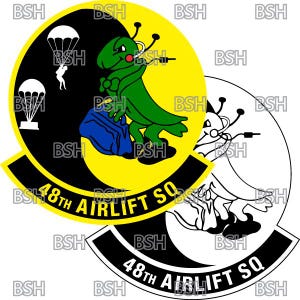 May include: A black and yellow circular patch featuring a green cartoon creature carrying a blue bag. The creature has a red ear and is holding a microphone. The text "48th AIRLIFT SQ" is written in a black arc around the creature.