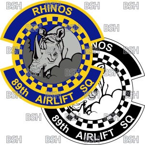 以下が含まれることがあります： 「RHINOS 89th AIRLIFT SQ」という文字と白黒のサイのイラストが描かれた青と黄色の円形のワッペン。ワッペンは縁に市松模様があります。