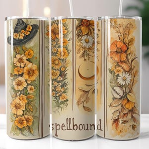 Puede incluir: Un juego de tres vasos de acero inoxidable con diseños florales y temáticos de brujas. Los diseños incluyen un sombrero de bruja, flores amarillas, una luna creciente y la palabra "spellbound". Los vasos tienen una pajita.