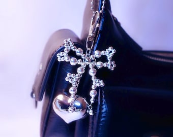 May include: A silver-toned heart-shaped charm with the inscription "welcome love" hangs from a beaded bow-shaped accent. The charm is attached to a black leather handbag with a silver chain.