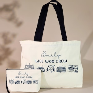 May include: A cream-colored canvas tote bag and a matching zippered pouch, both featuring black handles and a dark blue graphic print. The design includes the name Emily, the text WEE WOO CREW, and illustrations of emergency vehicles and gear.