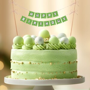 May include: A green and white cake decorated with green and silver balls and a banner that says "Happy Birthday".