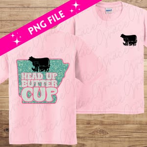 May include: Pink t-shirt with a graphic design of a cow and calves in front of an outline of the state of Arkansas. The text "Head Up Butter Cup" is written in pink and green letters.