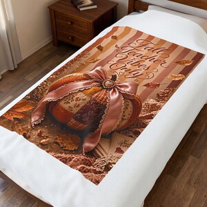 Puede incluir: Una manta blanca con un diseño estampado de una calabaza de patchwork con un gran lazo de satén rosa, rodeada de hojas de otoño y rayas marrones. El texto Fall Teacher Vibes Only está impreso en una fuente cursiva de color marrón.
