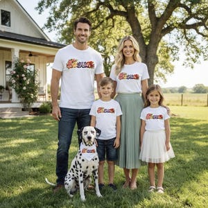 Puede incluir: Una familia de cuatro personas viste camisetas blancas a juego con la palabra JESUS impresa en una fuente floral colorida, combinadas con pantalones vaqueros, pantalones cortos y una falda plisada, junto a un dálmata con un pañuelo blanco a juego.