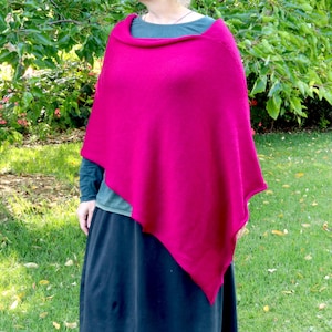 May include: A bright pink knitted poncho with a simple design. The poncho is made of a soft, comfortable fabric and has a relaxed fit.