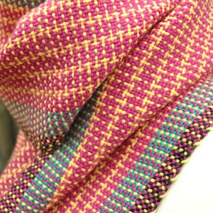 May include: A pink, yellow, and teal woven scarf with a geometric pattern.