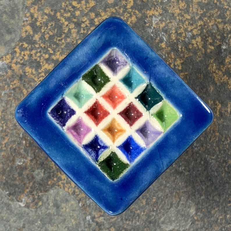 Puede incluir: Un azulejo de cer&aacute;mica azul con un patr&oacute;n de diamante. Los diamantes est&aacute;n rellenos de diferentes colores, incluyendo rojo, verde, amarillo, morado y azul.