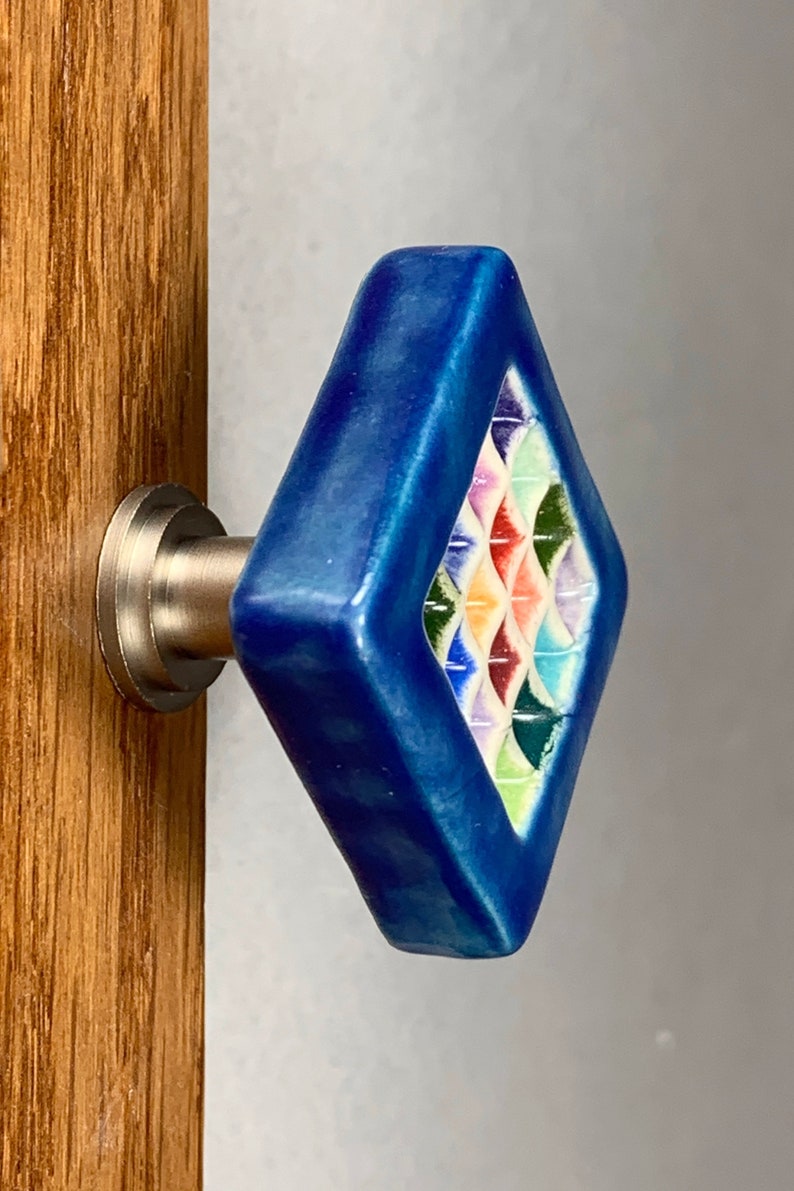 Puede incluir: Un pomo de armario de cer&aacute;mica azul con un dise&ntilde;o geom&eacute;trico colorido. El pomo est&aacute; unido a una base de metal plateado.