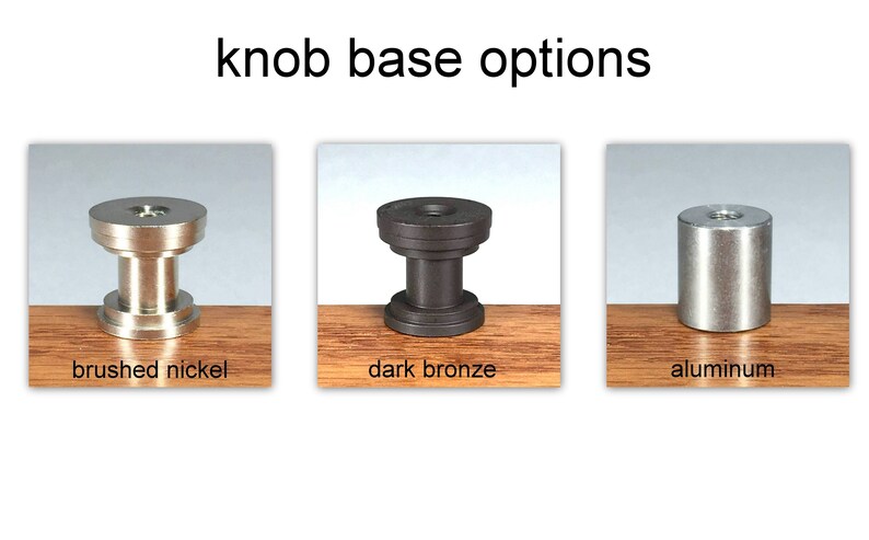 Puede incluir: Tres bases de pomo diferentes en n&iacute;quel cepillado, bronce oscuro y aluminio. Las bases se muestran sobre una superficie de madera.