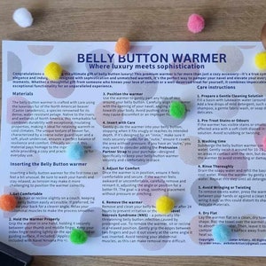 May include: A product display featuring a printed sheet with instructions for a "Belly Button Warmer," a small wooden box, a black box, and colorful pom-poms scattered on a wooden surface. The text on the sheet reads "Belly Button Warmer where luxury meets sophistication."