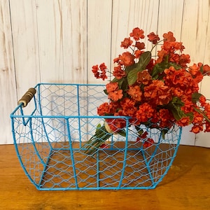 Puede incluir: Una cesta de alambre azul con un asa de madera, llena de un ramo de flores naranjas.