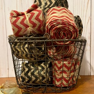 May include: A wire basket filled with rolls of burlap ribbon in red, black, and natural colors. The ribbon has a chevron pattern.