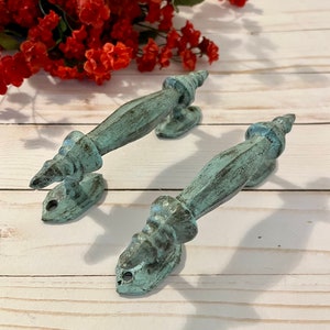 May include: Two antique-style door pulls with a distressed turquoise finish. The pulls have a decorative, ornate design and are made of metal.